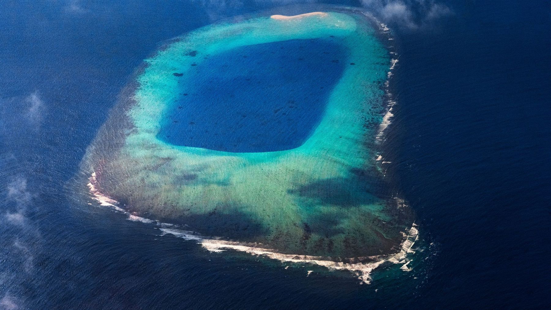 Un atolón coralino visto desde el aire: un anillo de arrecife y arena alrededor de una laguna poco profunda, la forma que da a Taka Bonerate su nombre y su estructura.